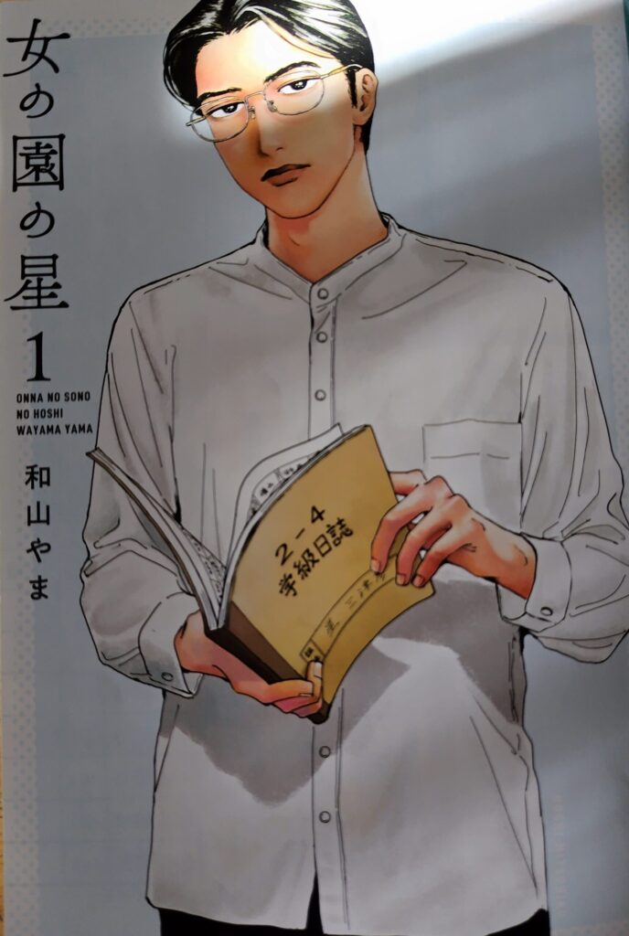 メガネをかけた星先生が「2-4 学級日誌」を手に持ち、落ち着いた表情で立つ学園漫画『女の園の星』第1巻の扉絵。星三津彦先生。