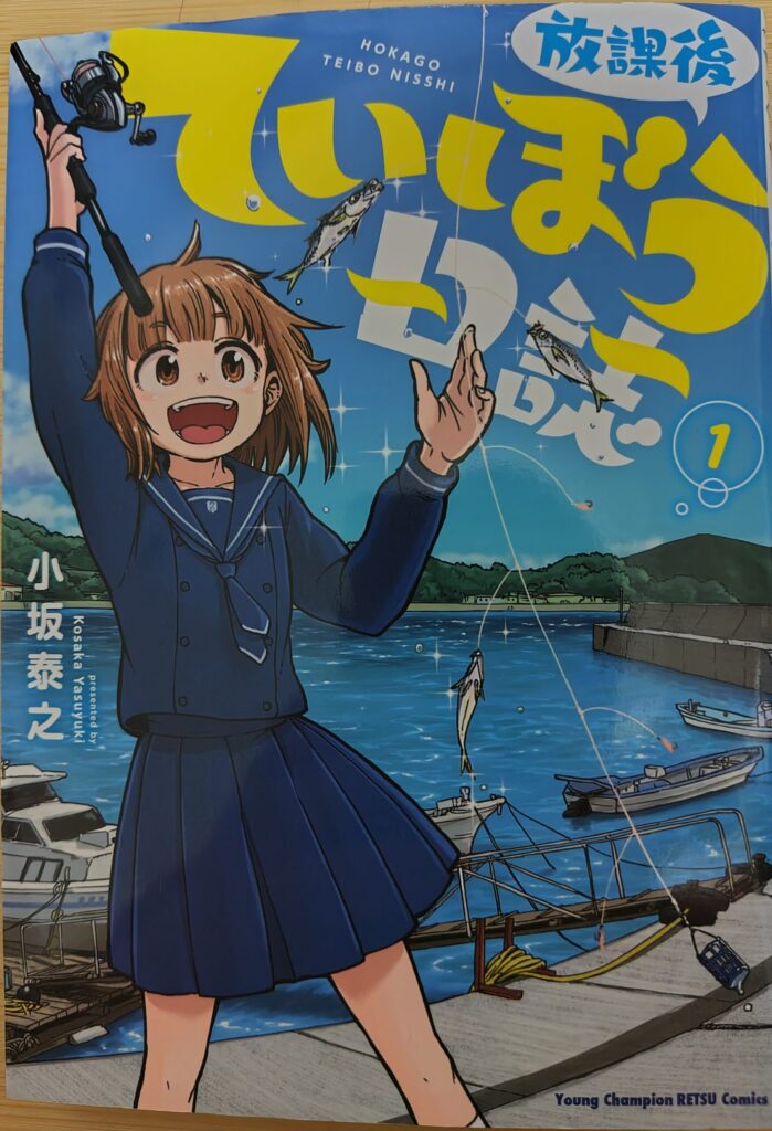 「『放課後ていぼう日誌』1巻の表紙。鶴木陽渚が釣り竿を持ち、魚を釣り上げて笑っているシーン。