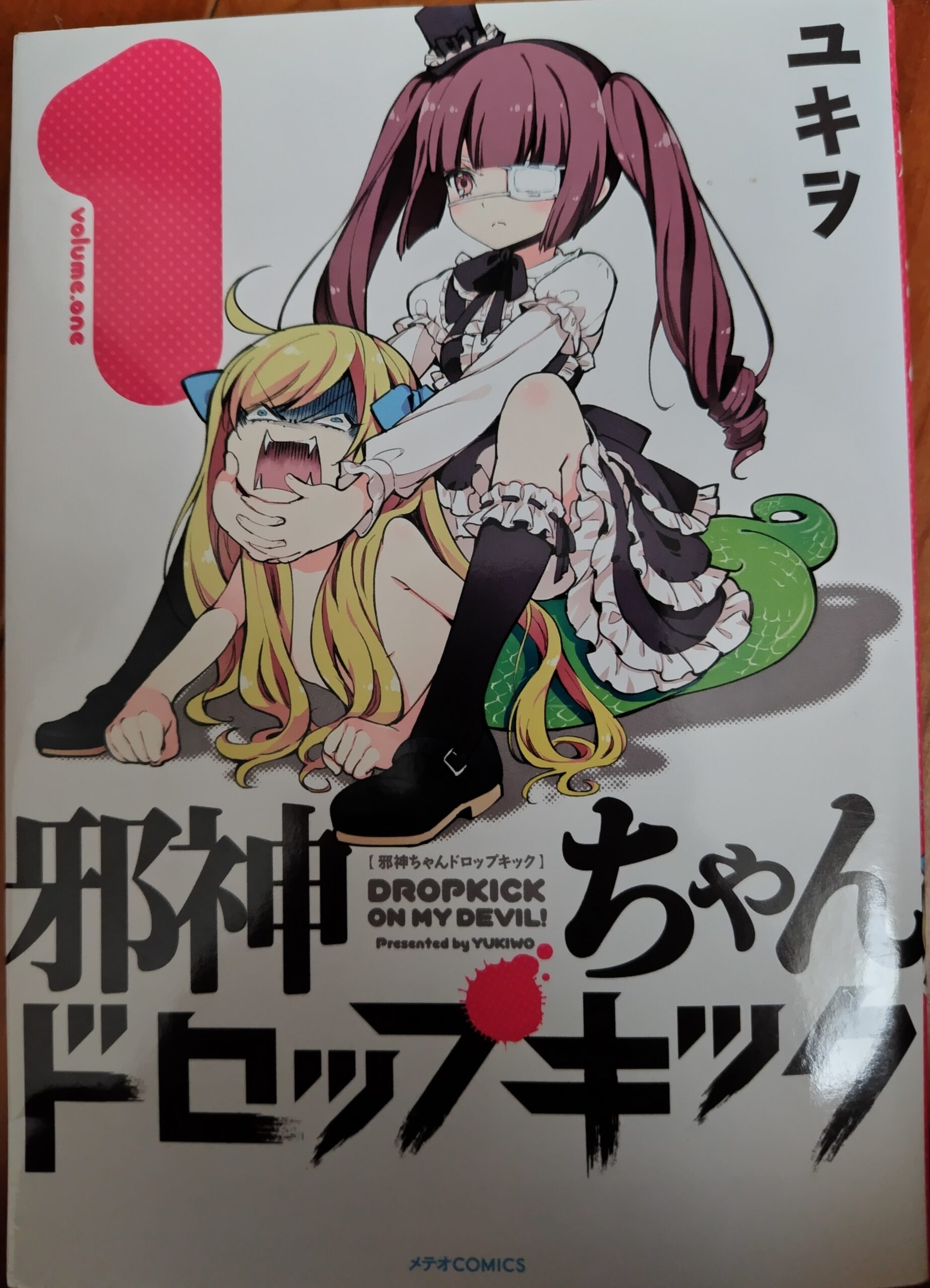 『邪神ちゃんドロップキック』1巻の表紙で、花園ゆりねが邪神ちゃんにガチめのキャメルクラッチをキめているシーン。