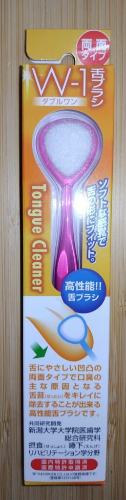 W-1舌ブラシのパッケージ写真。ピンクの持ち手と白いブラシ面が特徴で、舌苔を優しく除去する両面タイプの舌クリーナー。口臭の主な原因となる舌苔を効果的に取れることが強調されている。