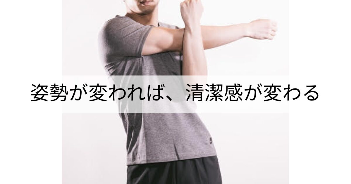 グレーのTシャツと黒のショーツを着た男性が、腕を胸の前で伸ばす肩ストレッチをしている様子。